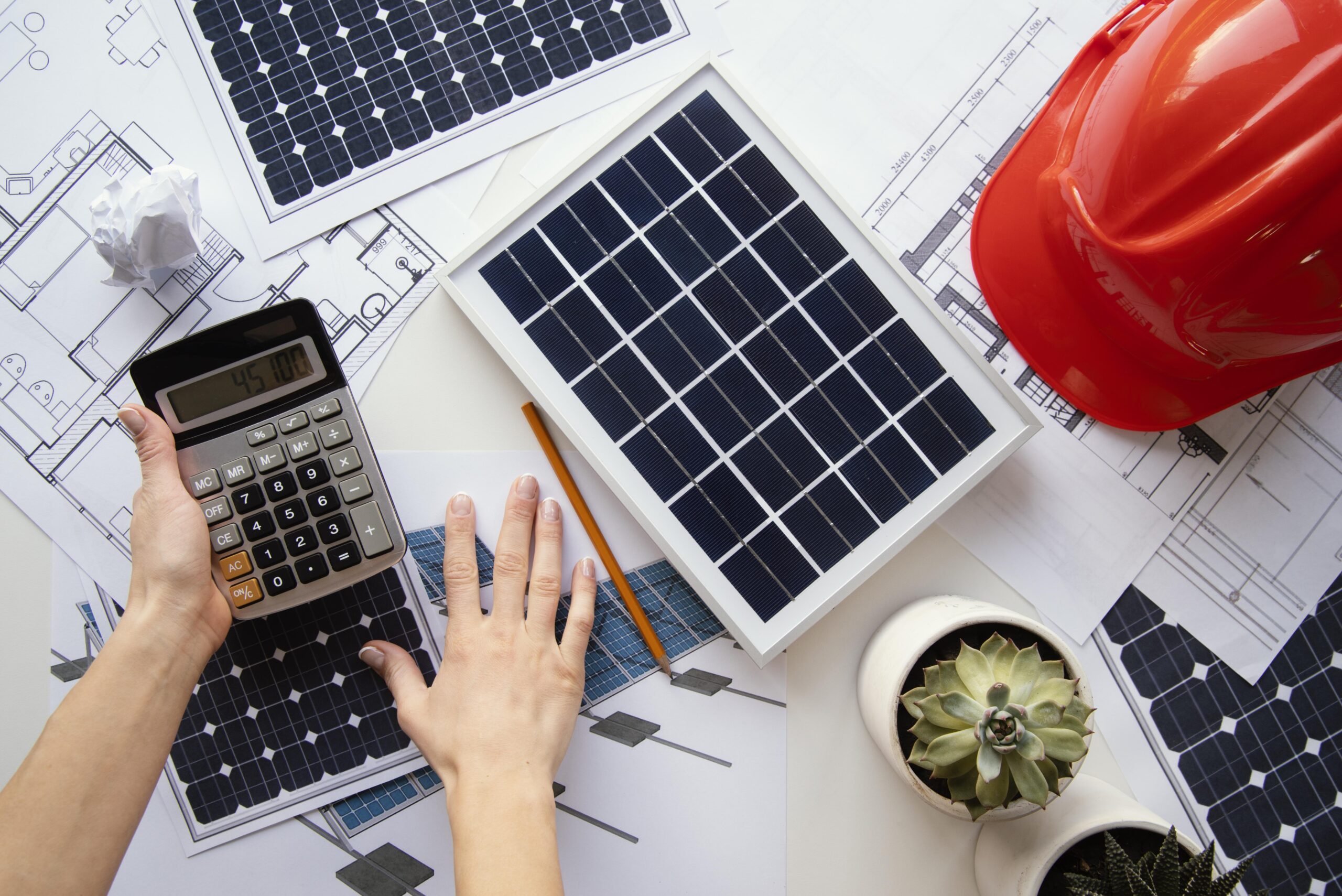 Person mit Taschenrechner über Plänen und kleinen Solarmodulen – Symbolbild