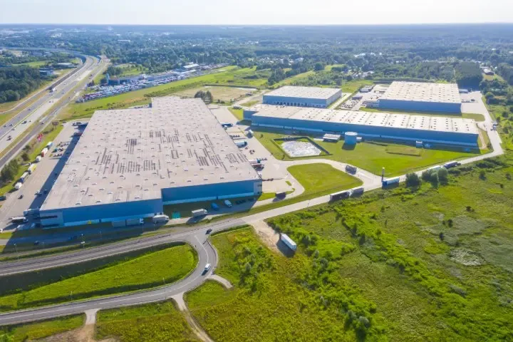 Luftaufnahme eines Logistikgebiets mit Solarmodulen auf großen Hallendächern und Lkw an den Rampen
